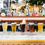 A row of five beer glasses in various colours on a marble bar, showcasing different beer styles.