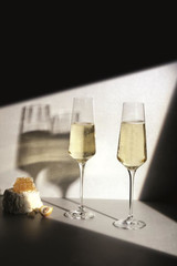 Two elegant crystal champagne flutes with a light golden beverage, alongside a piece of cheese and a honeycomb.