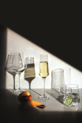 A collection of glass tumblers in various shapes, including tall flutes, set against a dark background with fruit.