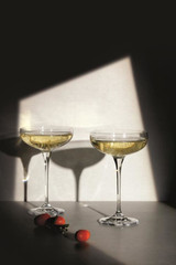 Two elegant champagne coupe glasses filled with bubbly drink, set against a dark background with a playful shadow.