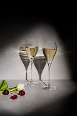 Elegant transparent flute glasses filled with sparkling beverage, accompanied by cherries and flowers on a textured surface.