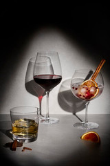 A set of three elegant glasses: a whisky glass, a wine glass, and a large cocktail glass with garnishes, against a dark background.