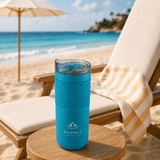 A drink bottle in vibrant blue, featuring a textured grip and a clear lid, set on a beachside chair.