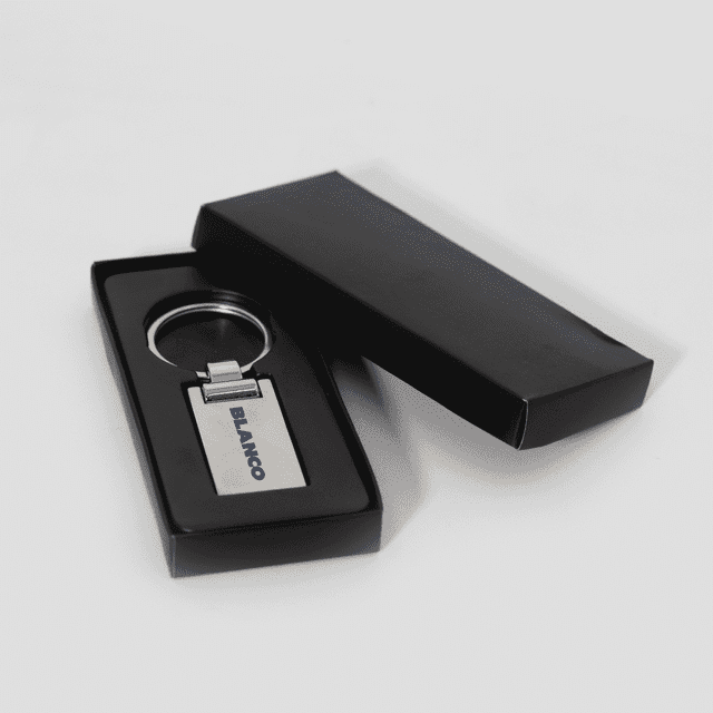 A silver keychain in a black presentation box, featuring a simple design and a logo.