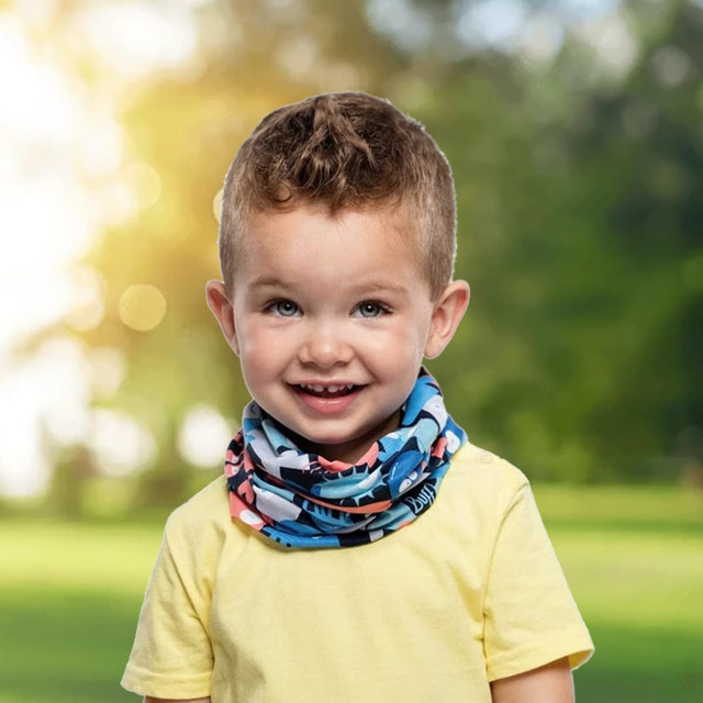 A smiling child wearing a blue and pink patterned Coolmax bandana outdoors, with greenery in the background.