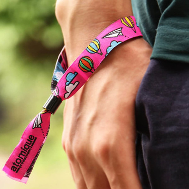 A pink wristband featuring colourful designs of balloons and paper planes, secured on a person's wrist.