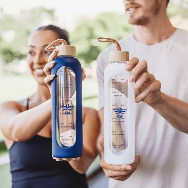 A drink bottle in blue and a white drink bottle, both featuring a logo and a straw top, held by two people outdoors.