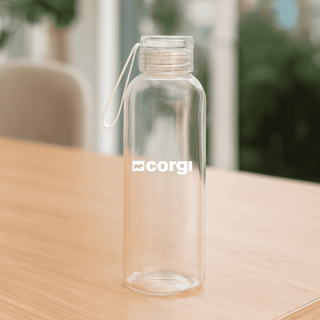 A drink bottle made of clear borosilicate glass with a white logo and a looped lid, placed on a wooden table.