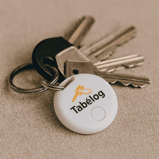 A set of keys with a white circular item tracker attached, featuring a logo on its surface.