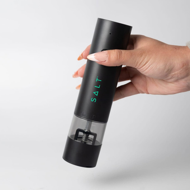 A rechargeable black pepper/salt grinder with a clear base, held in a hand. It features a branding logo.