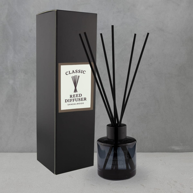 A round black glass reed diffuser with five black reeds, displayed beside a black box featuring a logo.