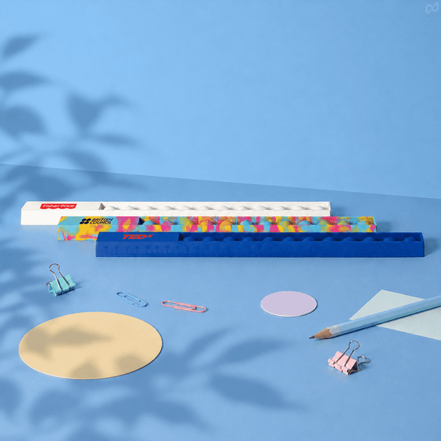 A 30cm popper ruler in blue with a colourful design, surrounded by stationery items like paperclips and circular paper.