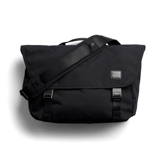 A black messenger bag with a flap, adjustable shoulder strap, and branding label. It features buckle closures and a sleek design.