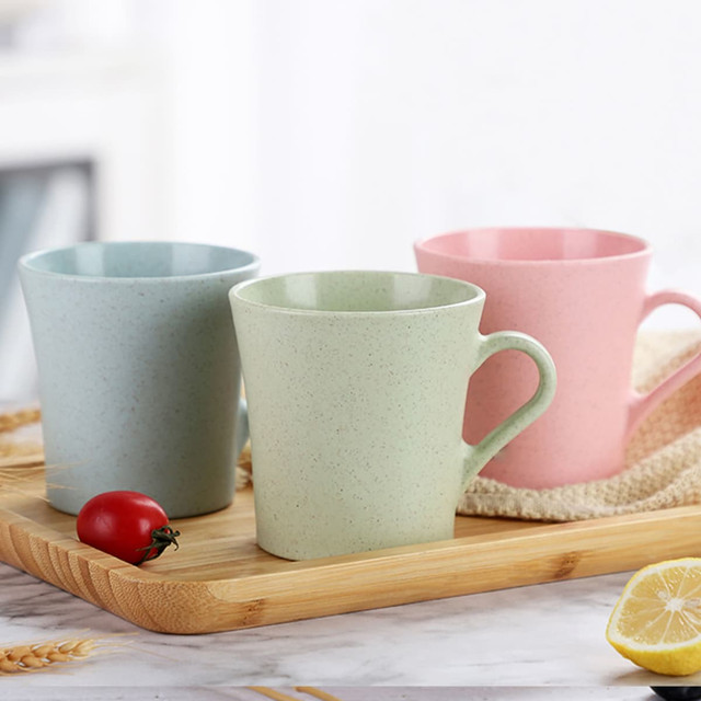 A drinkware set featuring three reusable coffee cups in green, blue, and pink, displayed on a wooden tray.