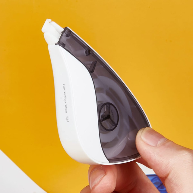A white and grey correction tape dispenser held by a hand against a bright yellow background.