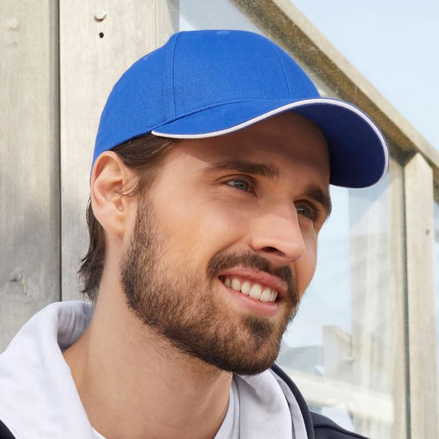 A blue six-panel heavy acrylic sandwich cap with a contrasting white trim, featuring a logo. A blue six-panel heavy acrylic sandwich cap with a contrasting white trim, featuring a logo.