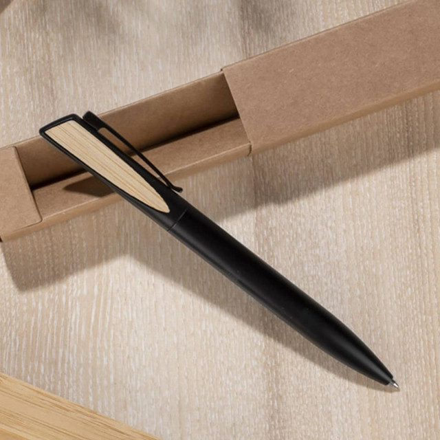 A black metal pen with a wooden accent, resting on a light wooden surface near a cardboard box.