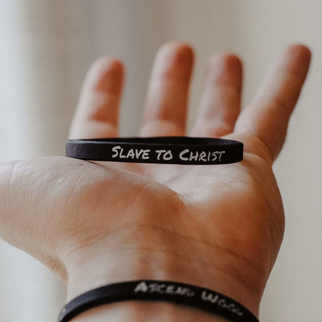 A hand holding a black silicone wristband with text, featuring another black wristband below it.