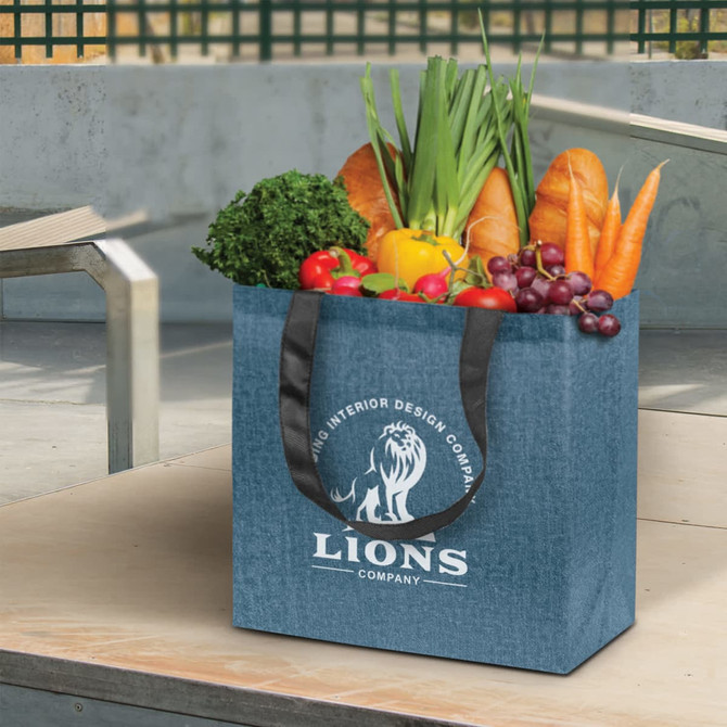 A blue tote bag filled with fresh vegetables and fruits, featuring black handles and a logo on the front.