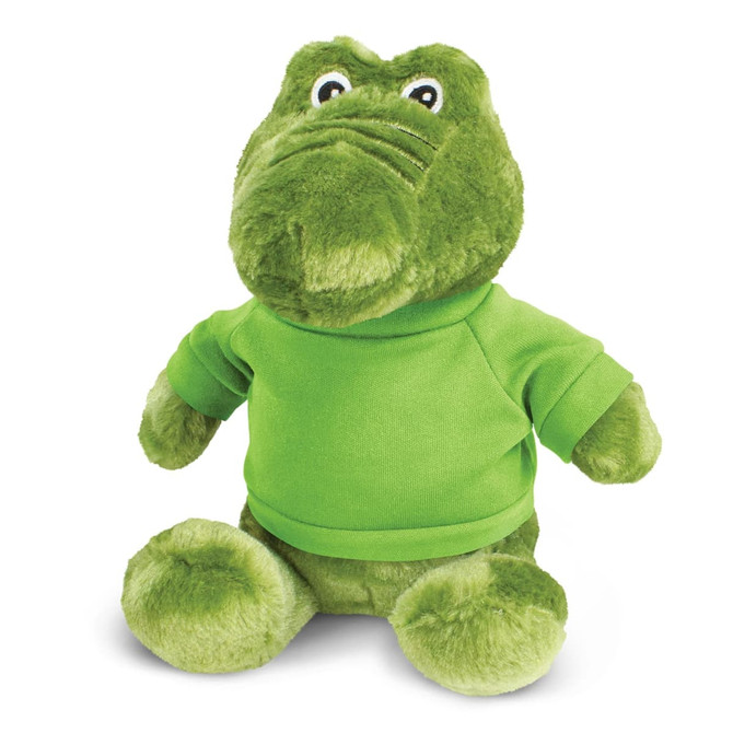 A green crocodile plush toy with a soft texture, wearing a green shirt, sitting upright. Features a logo on the shirt.