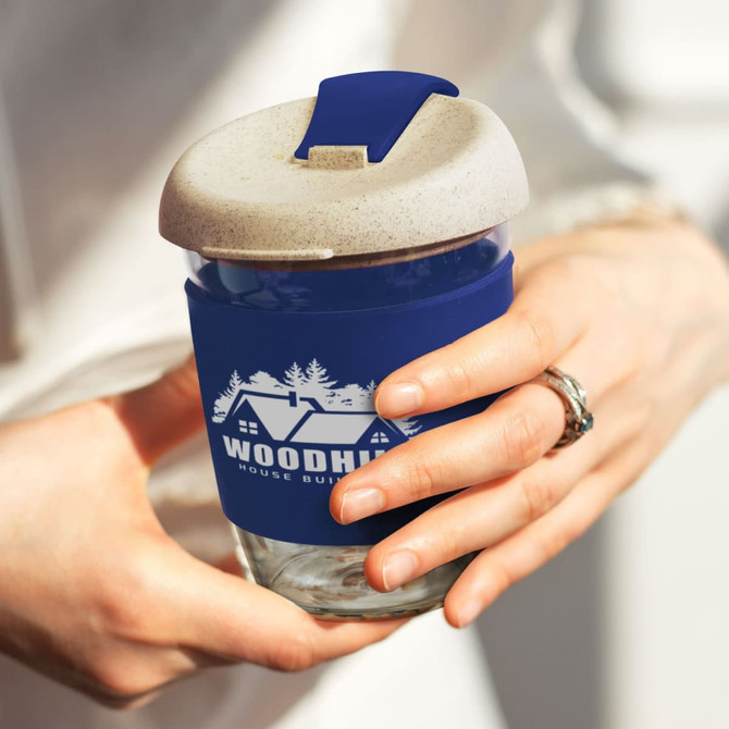 A drink bottle featuring a navy blue silicone sleeve and a natural-coloured lid, with a glass body and a logo.