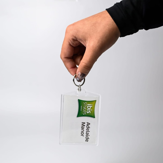 A hand holds a clear hotel keychain with a logo and a tag reading "Adelaide Manor." The keychain is transparent.