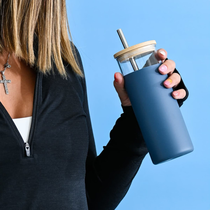 A drink bottle with a glass body and blue silicone sleeve, featuring a bamboo lid and stainless steel straw.
