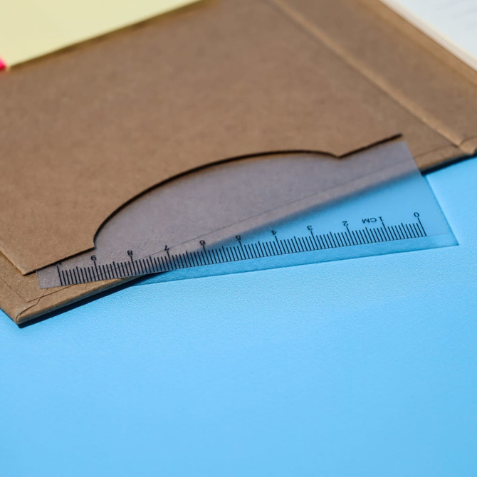 A clear plastic ruler with measurements rests on a brown notepad cover, featuring a simple design.