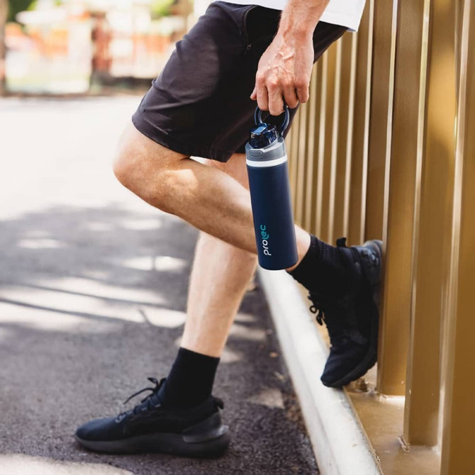 A drink bottle in navy blue held by a person, featuring a secure lid and a logo.