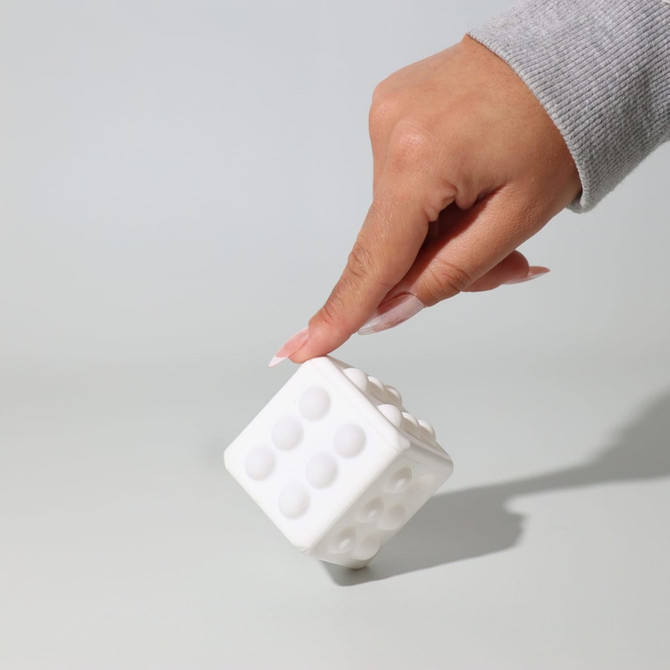 A white cube toy with rounded dots, being held by a hand, set against a light background.