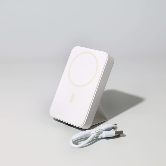 A white wireless charging power bank with a stand and a USB charging cable.