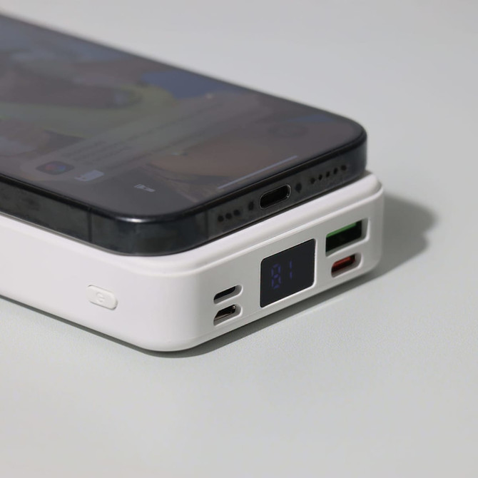 A white power bank with a digital display, featuring multiple ports, placed beside a smartphone.
