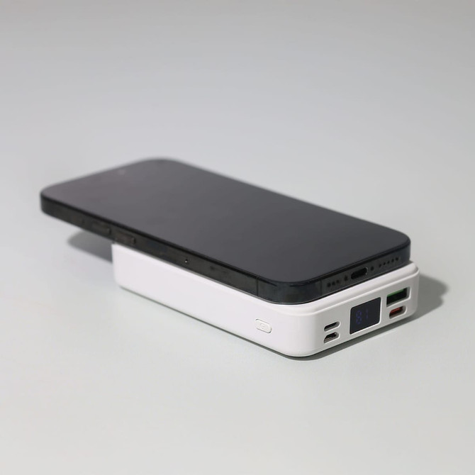 A black smartphone resting on a white Turbo 5000mAh wireless charging power bank with multiple ports.