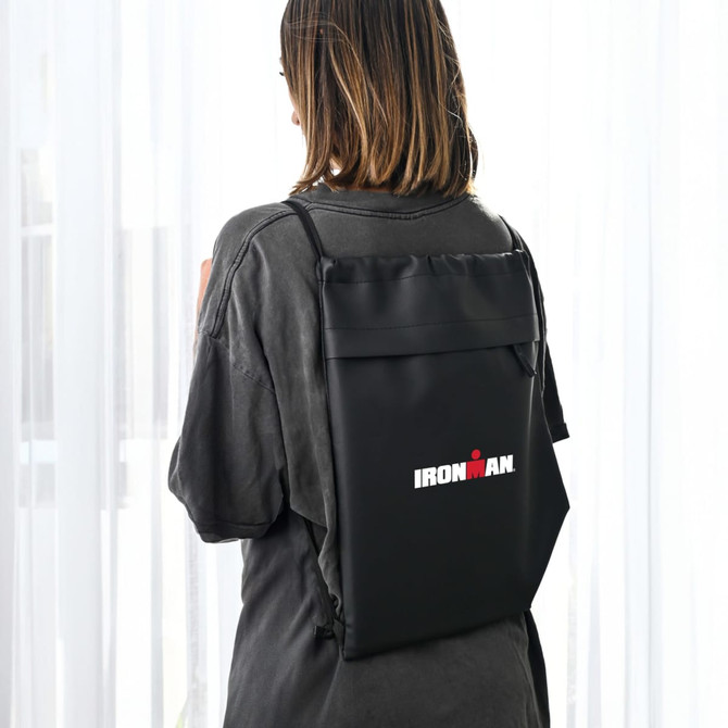 A black drawstring bag with a logo, worn on the back of a person, featuring a sleek design.
