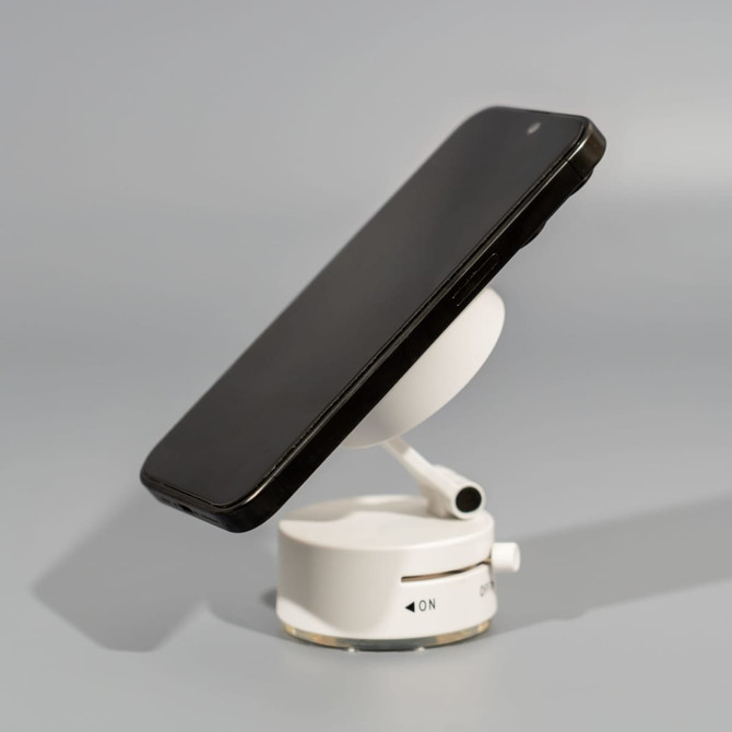 A white vacuum suction magnetic phone stand holding a black smartphone at an angle.