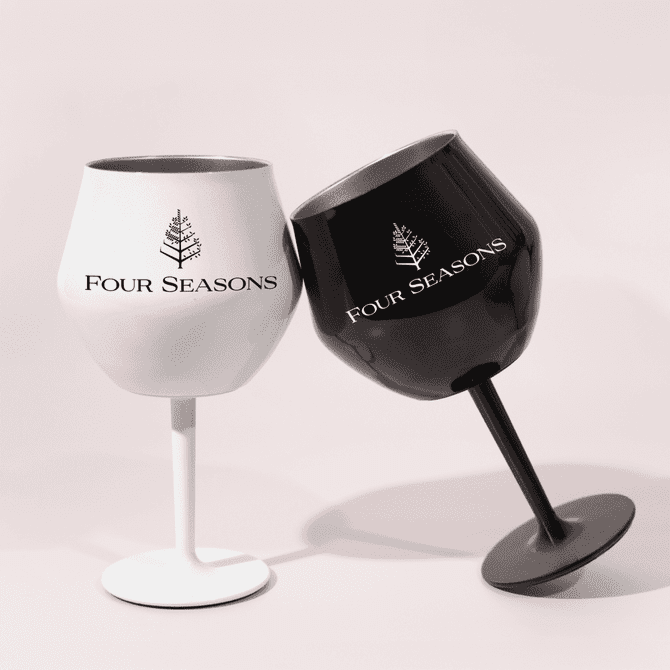 Two detachable wine glasses, one white and one black, featuring a logo on each, leaning towards each other.