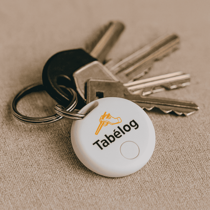 A set of keys with a white circular item tracker attached, featuring a logo on its surface.