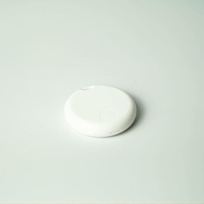 A round, white item tracker lies on a light surface, featuring a minimalistic design.