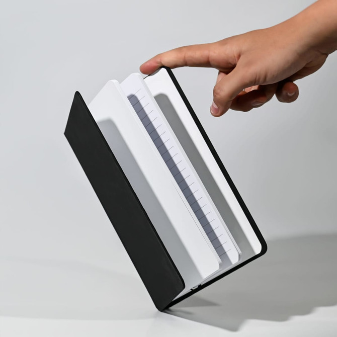A Polychroma A5 notebook with a black cover and white pages, being held by a hand, showcasing its design.