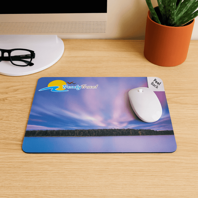 A mouse mat featuring a scenic purple and blue landscape with a logo and a white mouse on it, placed on a wooden desk.
