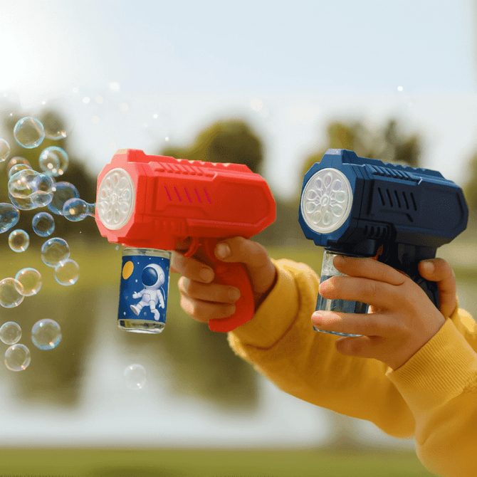 A red and blue bubble gun held by a child, with bubbles floating in the air and a scenic background.
