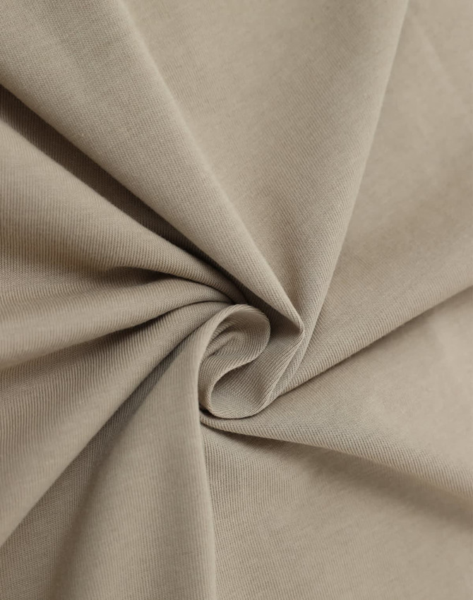 A close-up of soft, beige cotton fabric, showcasing its smooth texture and drape.