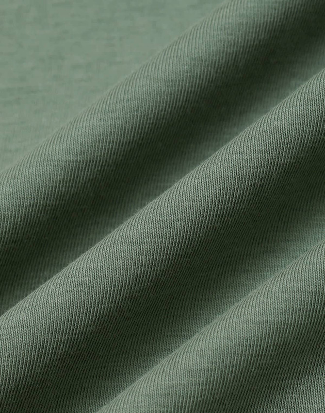 A close-up of folded fabric in a soft, muted green colour, showcasing a smooth texture with subtle ribbing.