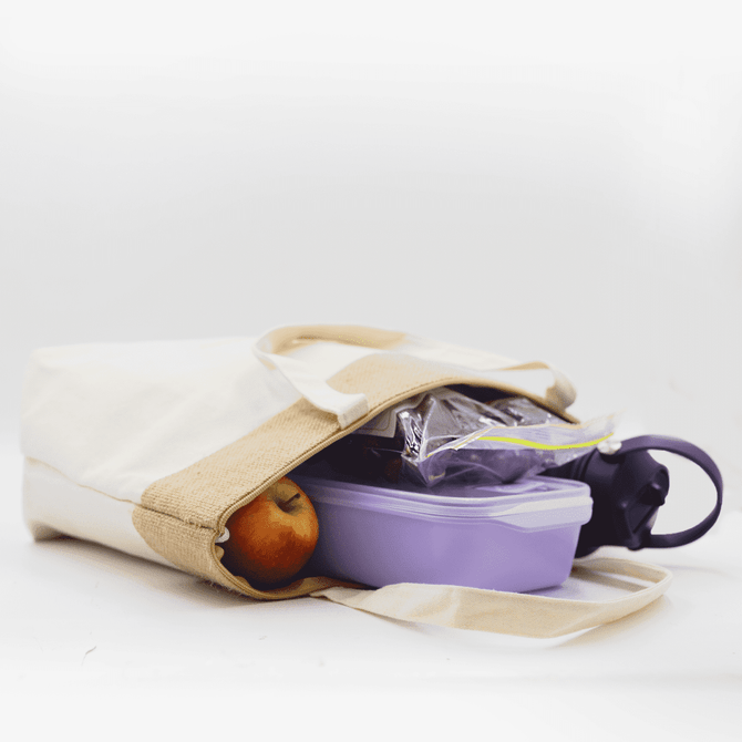 A jute and cotton cooler bag in cream and tan containing a drink bottle, a lunchbox, and an apple.