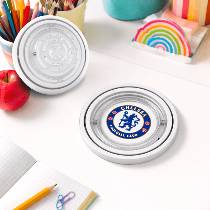 A circular coaster featuring a logo on a table, surrounded by stationery, an apple, and colourful paper.