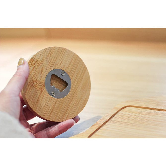 A drink bottle opener made from bamboo, featuring a round design and a metal bottle opener embedded in the centre.