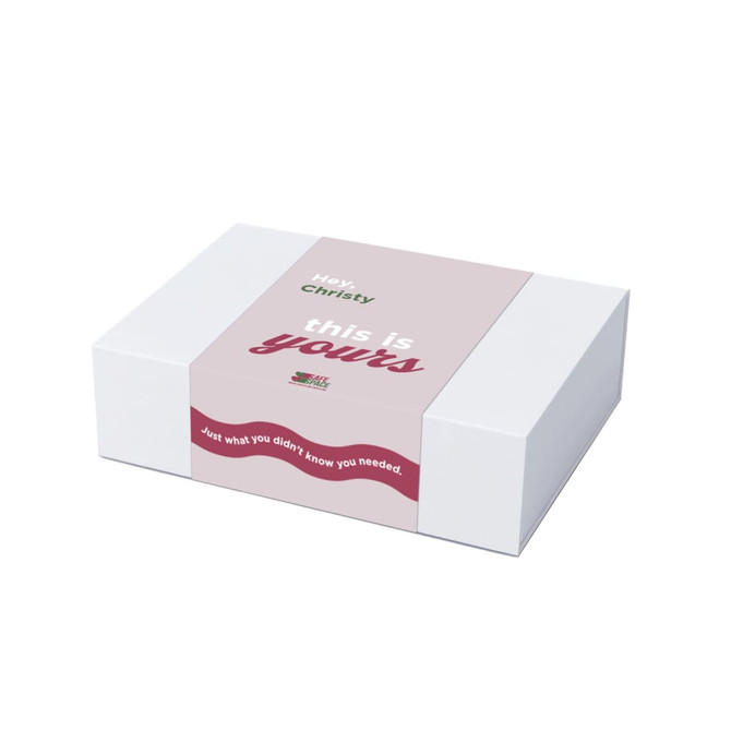 A white gift box with a pink and green label featuring a message and a decorative wavy design.