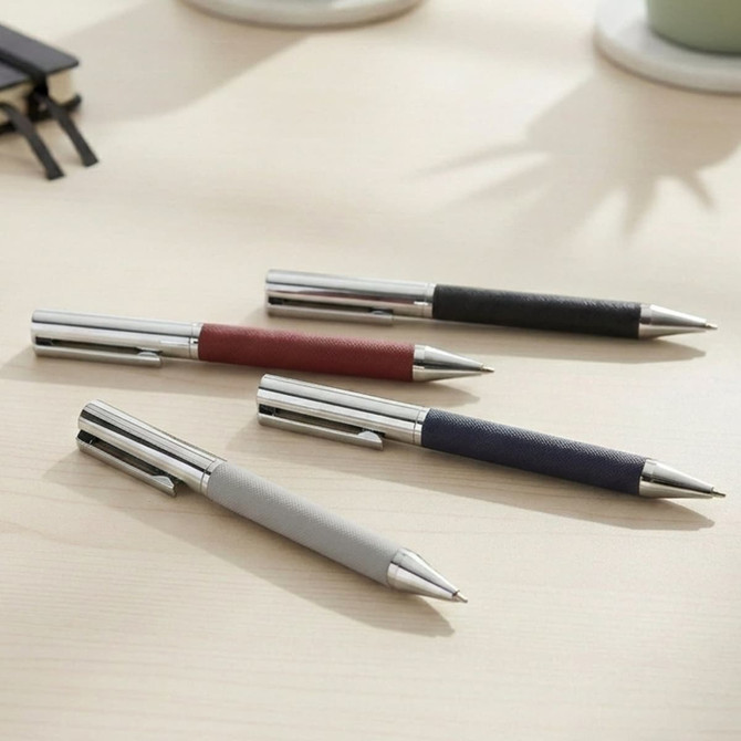 A collection of Geneva Metal Pens in grey, maroon, navy, and black with stainless steel accents, arranged on a desk.