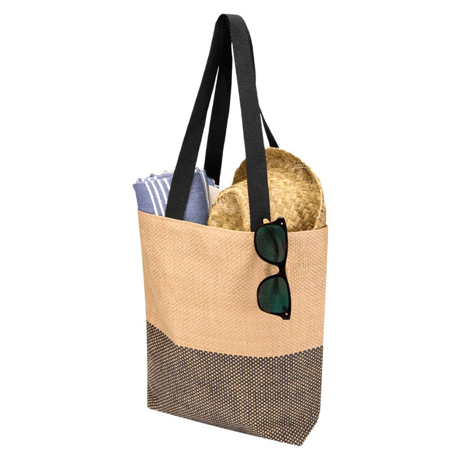 A beige and black tote bag with black straps, containing a towel and a straw hat, and sunglasses resting on the bag.