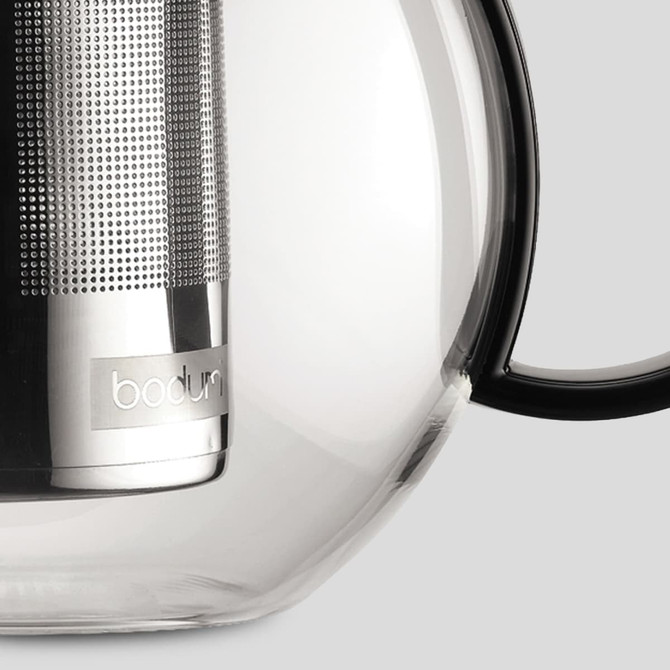 A glass tea press featuring a stainless steel infuser and a black handle, with a logo on the body.
